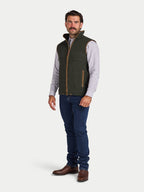Man wearing a green vest over a plaid shirt with blue jeans on a white background