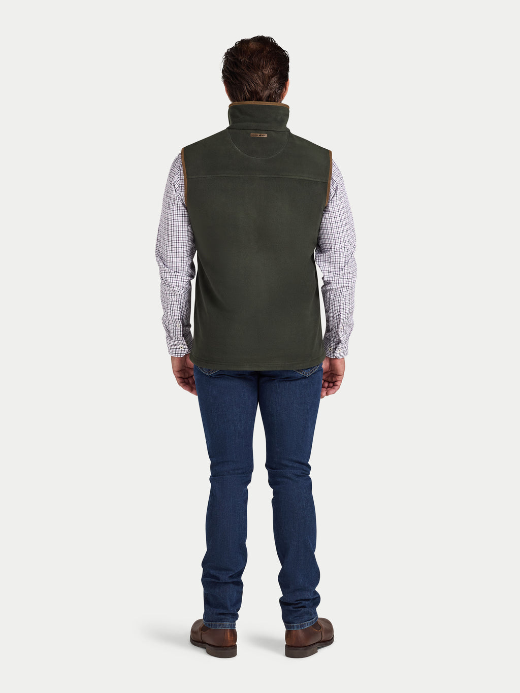 Man wearing a green vest over a plaid shirt with blue jeans on a white background