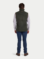 Man wearing a green vest over a plaid shirt with blue jeans on a white background
