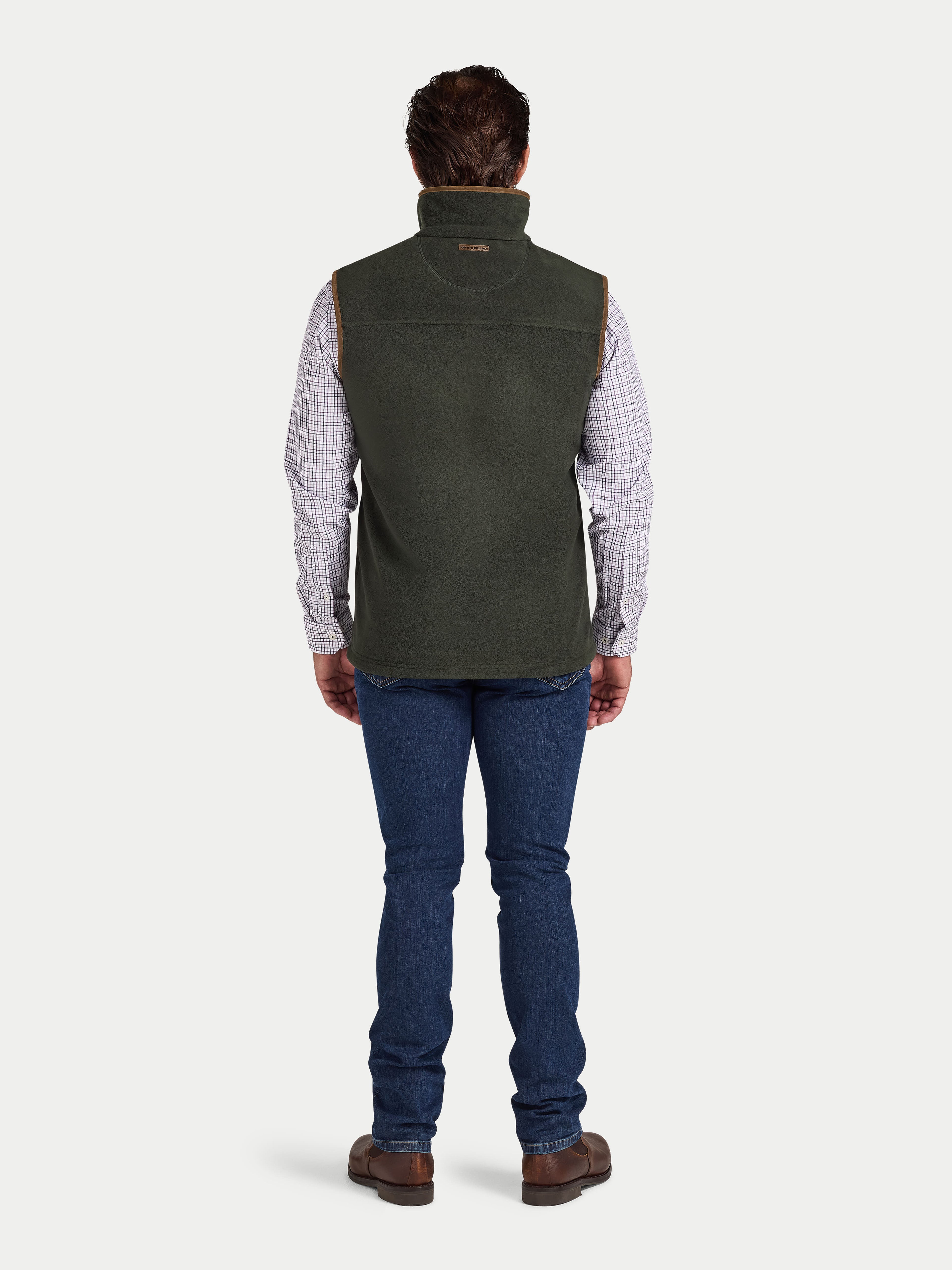 Man wearing a green vest over a plaid shirt with blue jeans on a white background