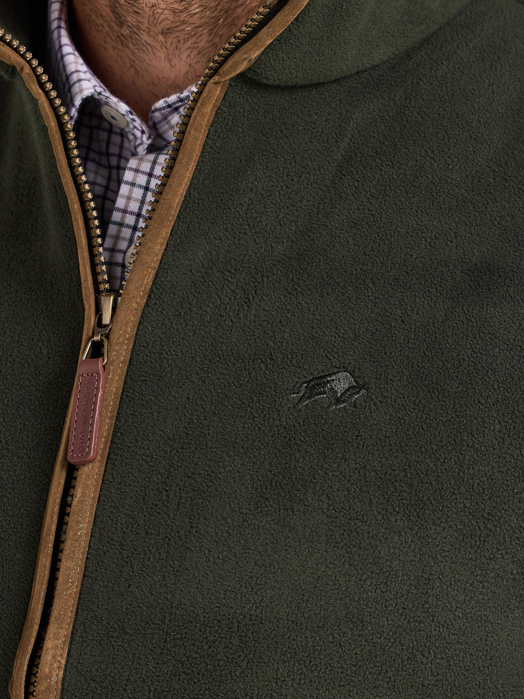 Green gilet with brown zipper and logo on a person wearing a checkered shirt.