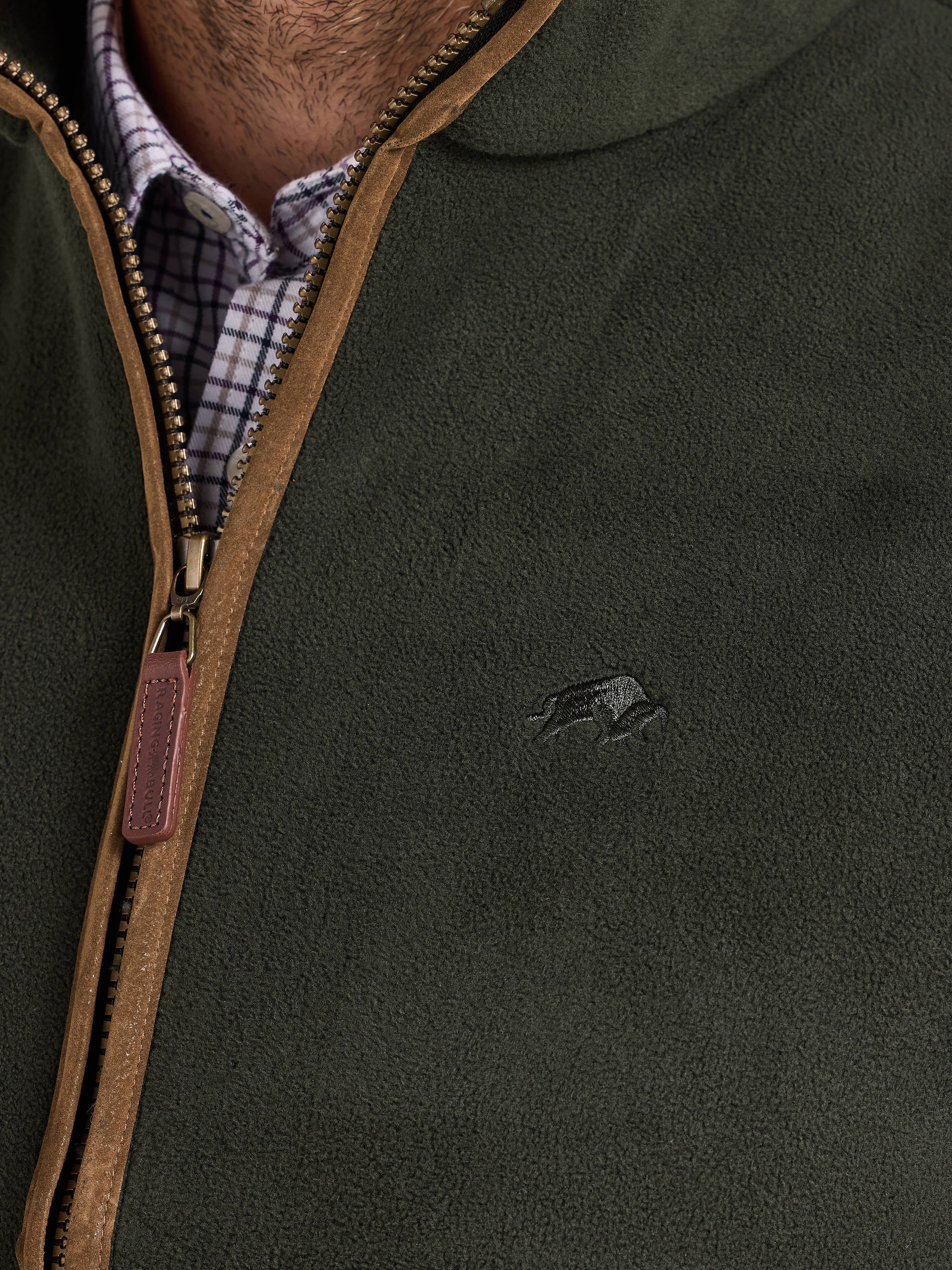 Green gilet with brown zipper and logo on a person wearing a checkered shirt.