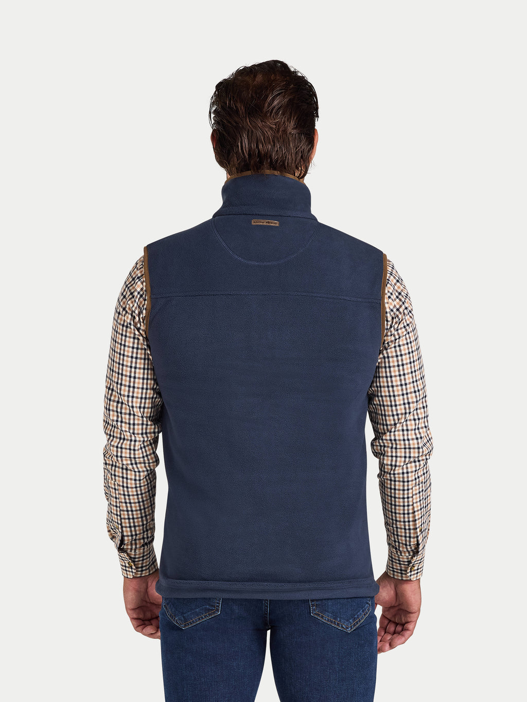 Man wearing a navy blue fleece gilet over a plaid shirt on a white background