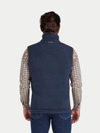 Man wearing a navy blue fleece gilet over a plaid shirt on a white background