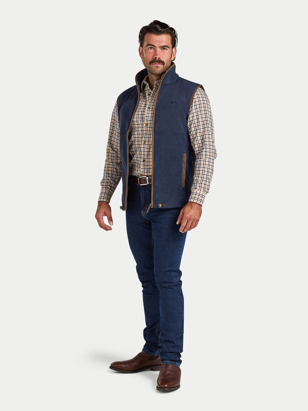 Man wearing a navy fleece vest over a plaid shirt with blue jeans on a white background