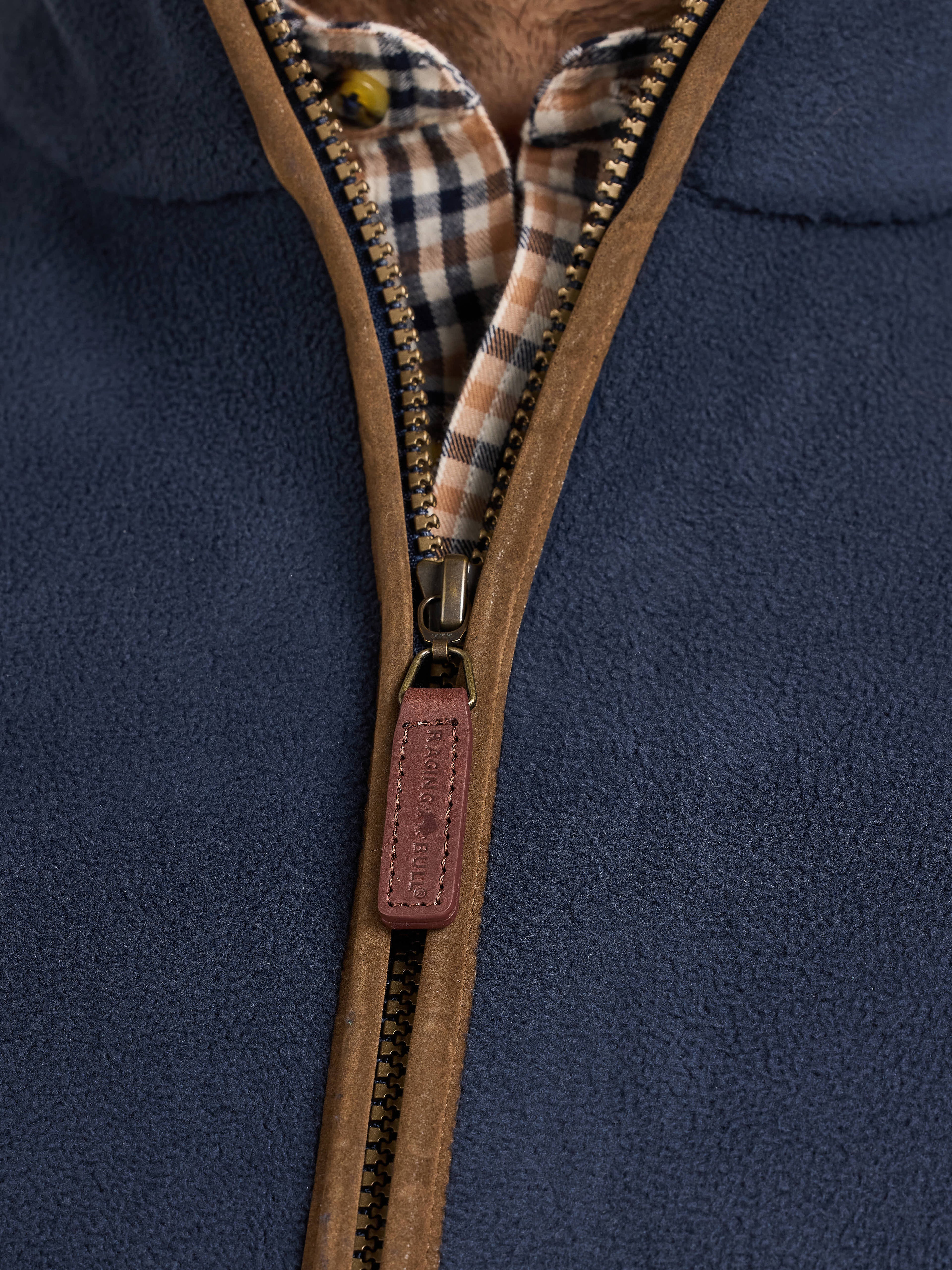 Close-up of a navy blue fleece gilet with a brown zipper and plaid lining.