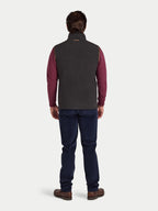 Person wearing a slate coloured gilet over a red shirt with blue jeans on a white background
