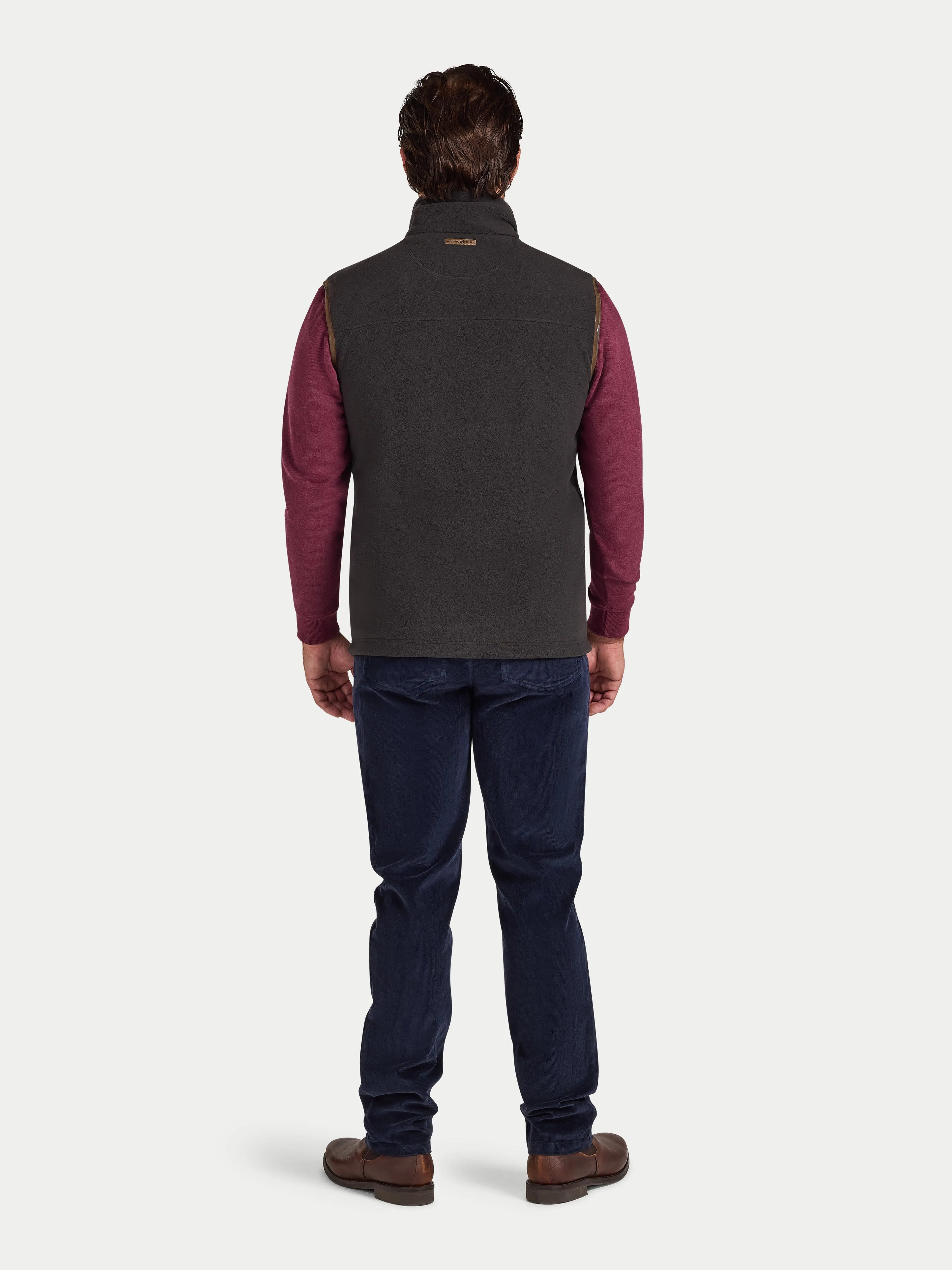 Person wearing a slate coloured gilet over a red shirt with blue jeans on a white background