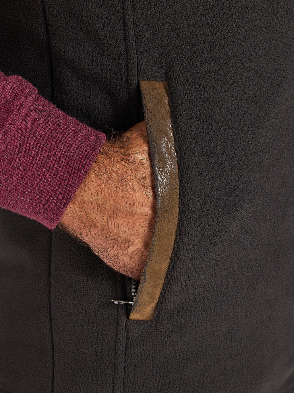 Close-up off a hand in a pocket of a slate coloured gilet.