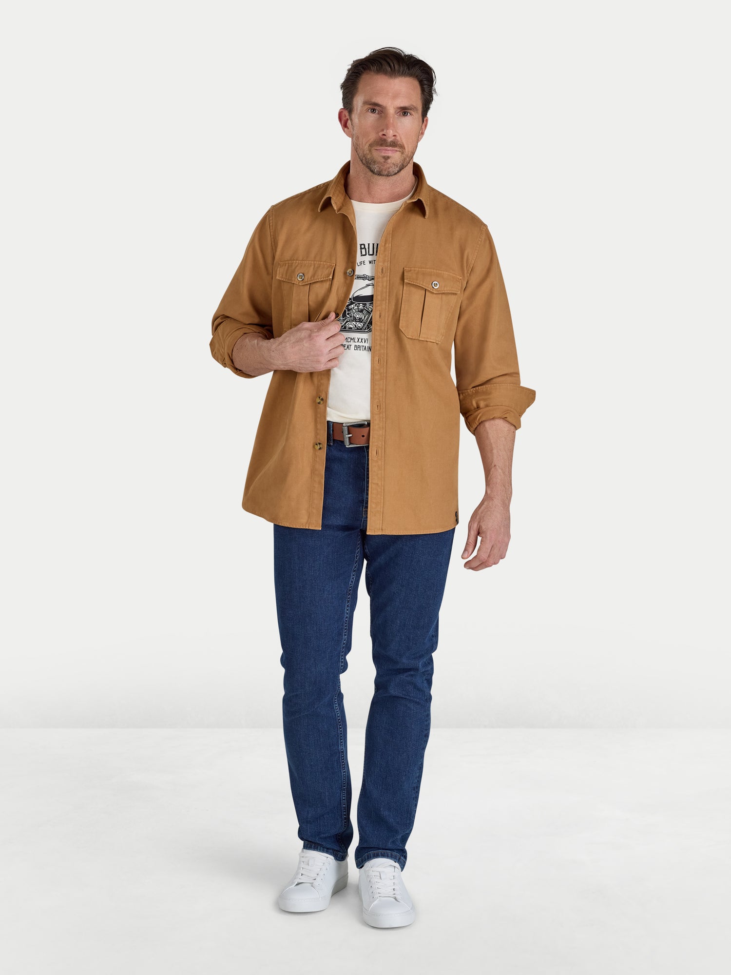Man wearing a brown shirt, white t-shirt, blue jeans, and white sneakers on a white background