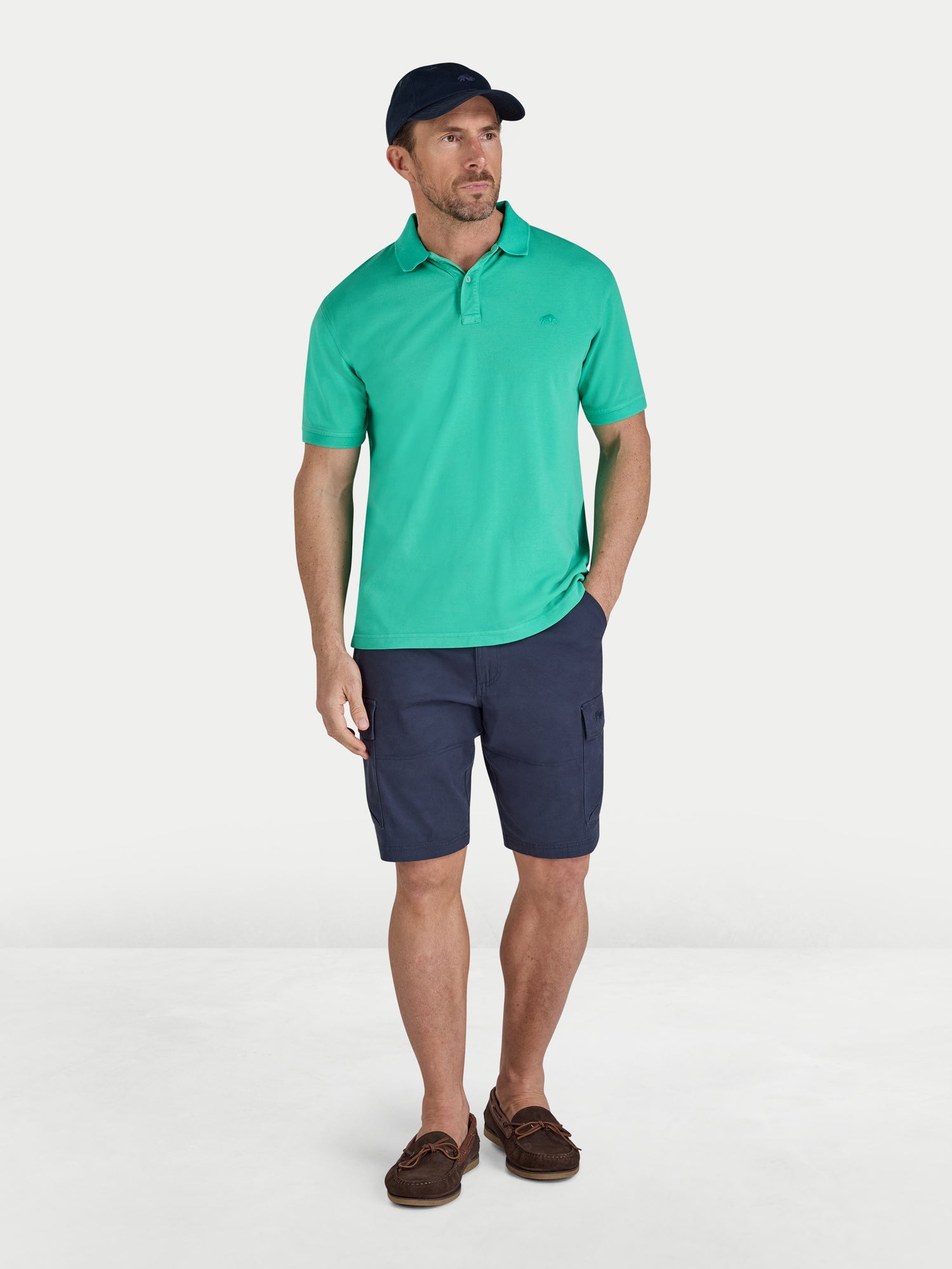 Man wearing a green polo shirt and navy shorts on a white background