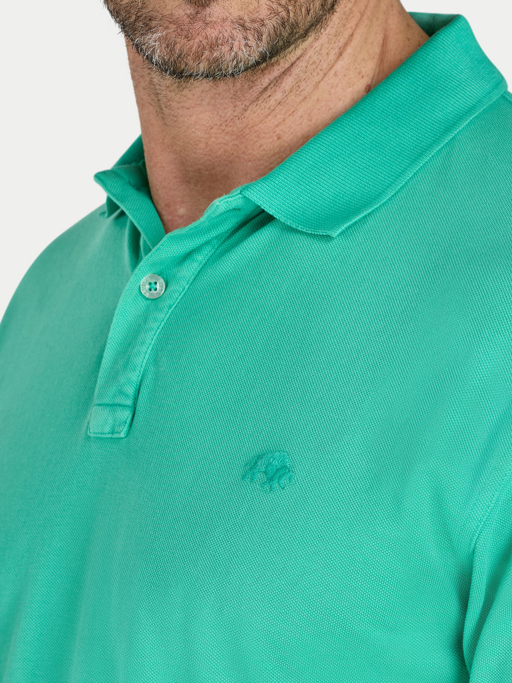 Close-up of a green polo shirt with a brand logo on a white background