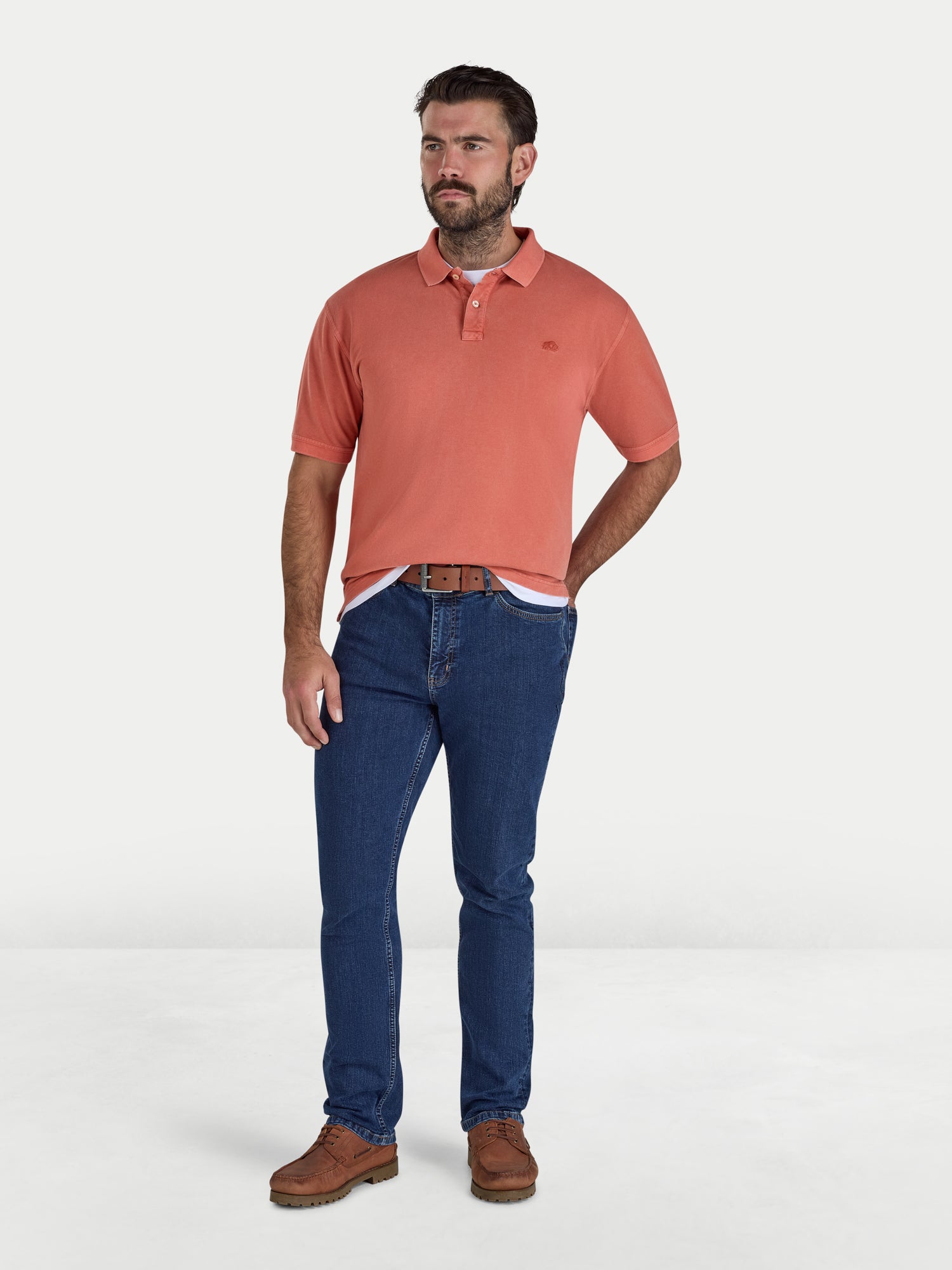 Man wearing an orangel polo shirt and blue jeans on a white background