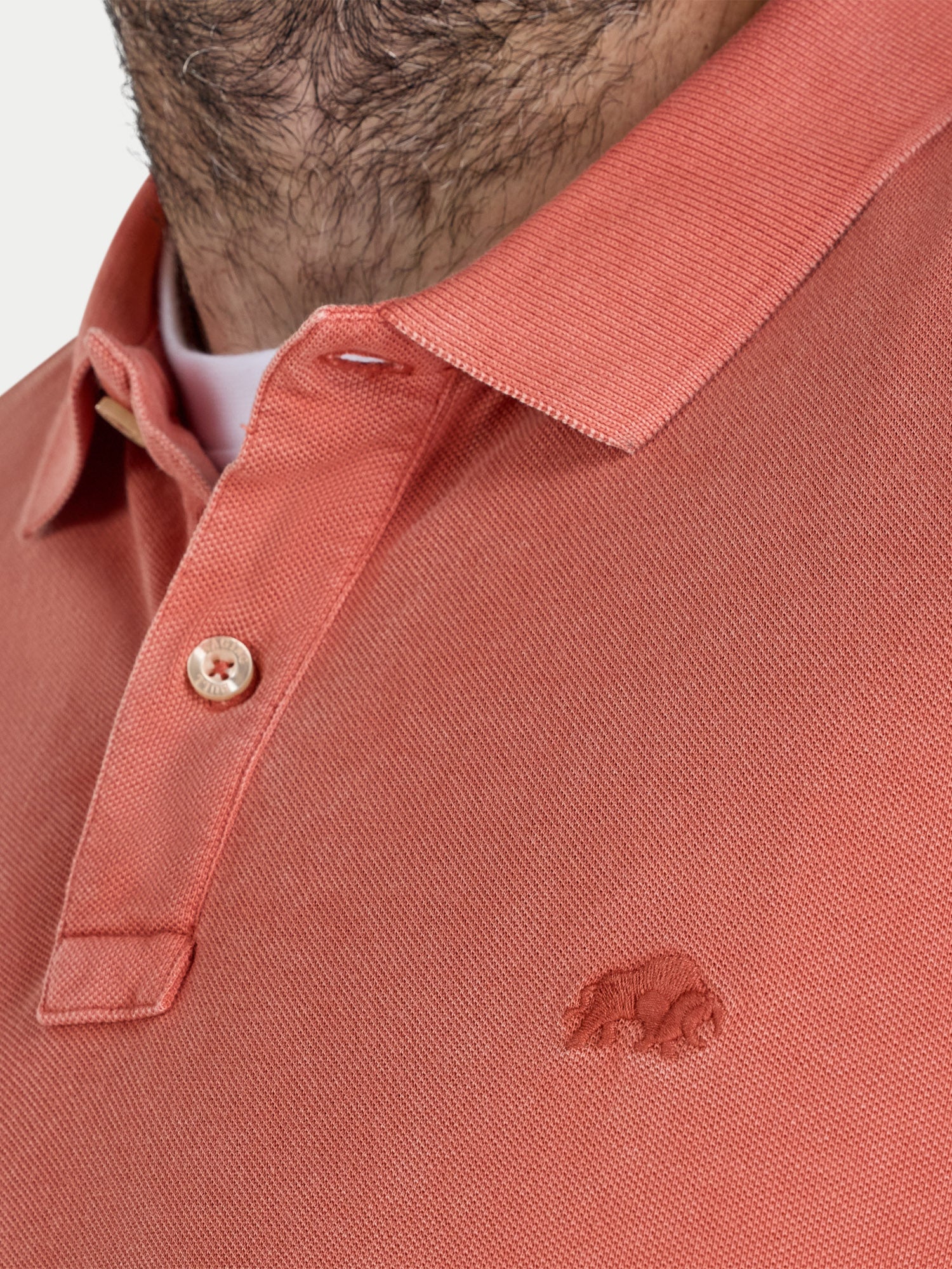 Close-up of a person wearing an orange polo shirt with a brand logo on a white background