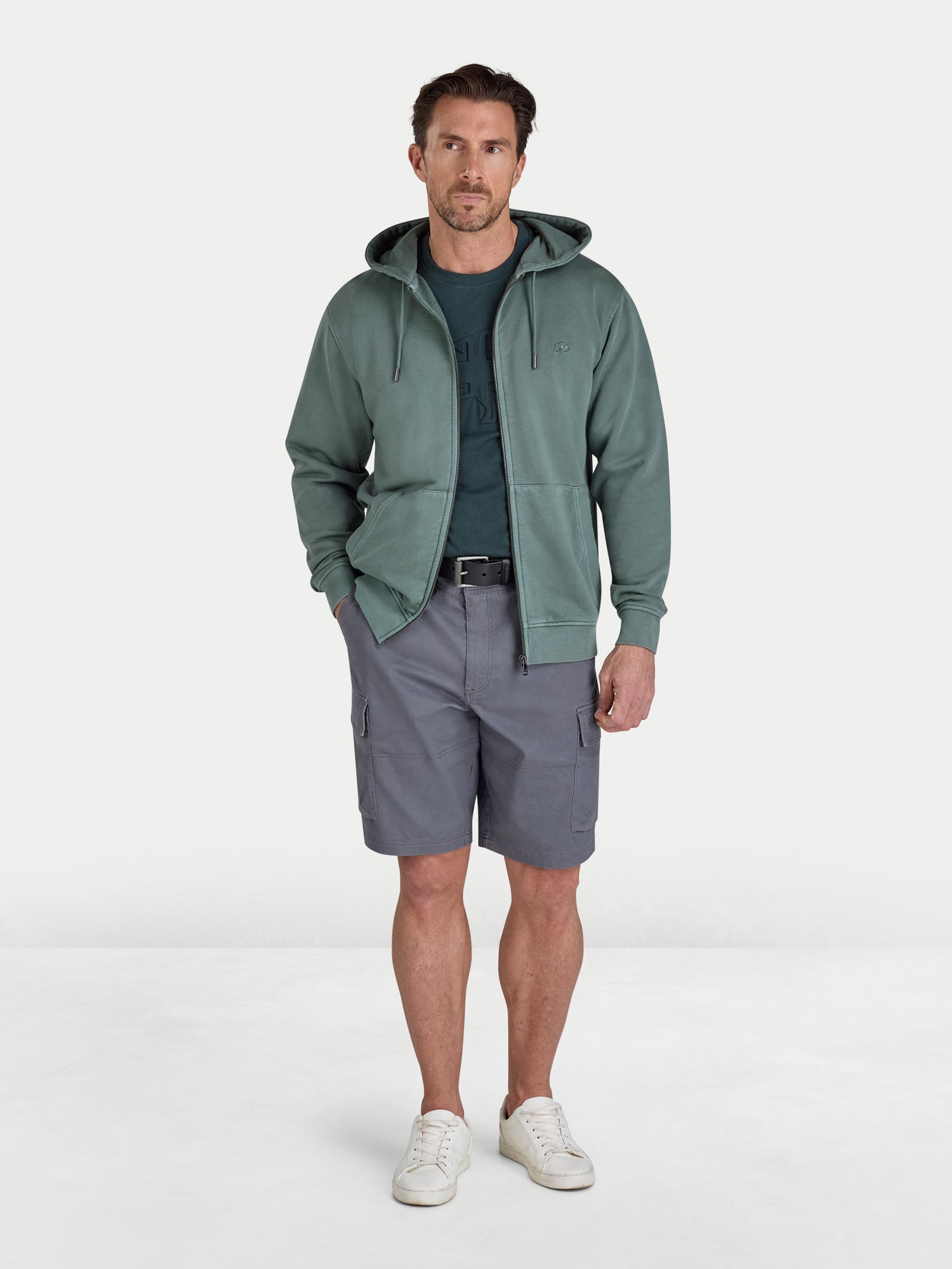 Man wearing a green hoodie, gray shorts, and white sneakers on a white background