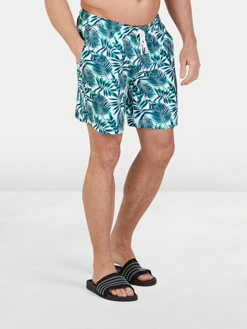 Person wearing tropical leaf patterned shorts on a white background