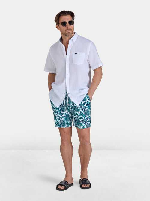 Man wearing a white shirt and leaf-patterned shorts on a white background