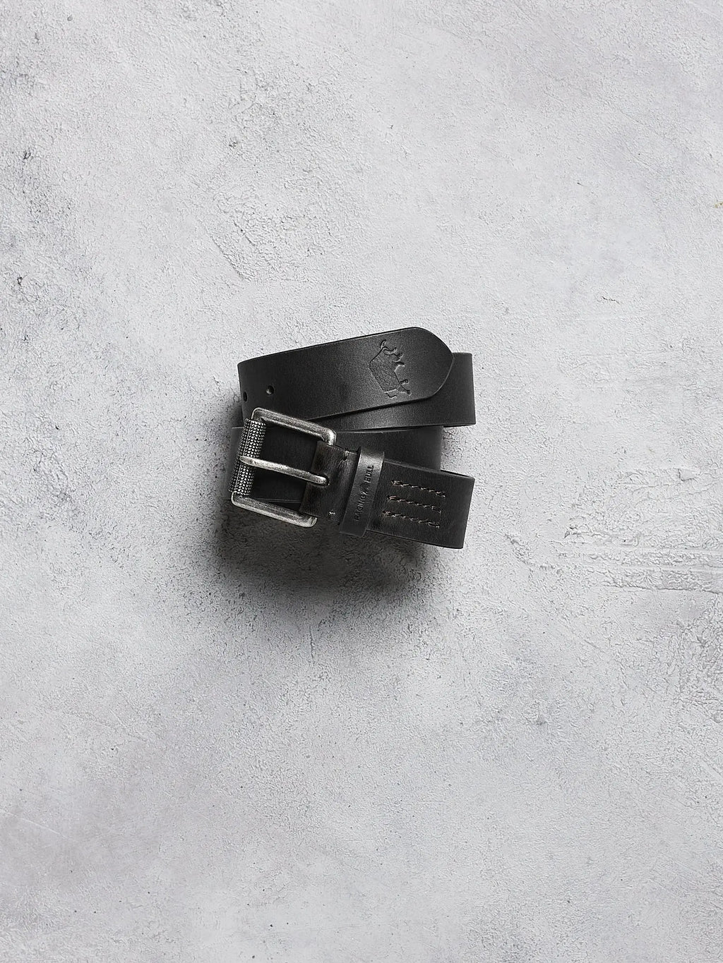 Black leather belt with silver buckle on a gray concrete surface