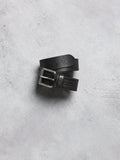 Black leather belt with silver buckle on a gray concrete surface