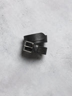 Black leather belt with silver buckle on a gray concrete surface