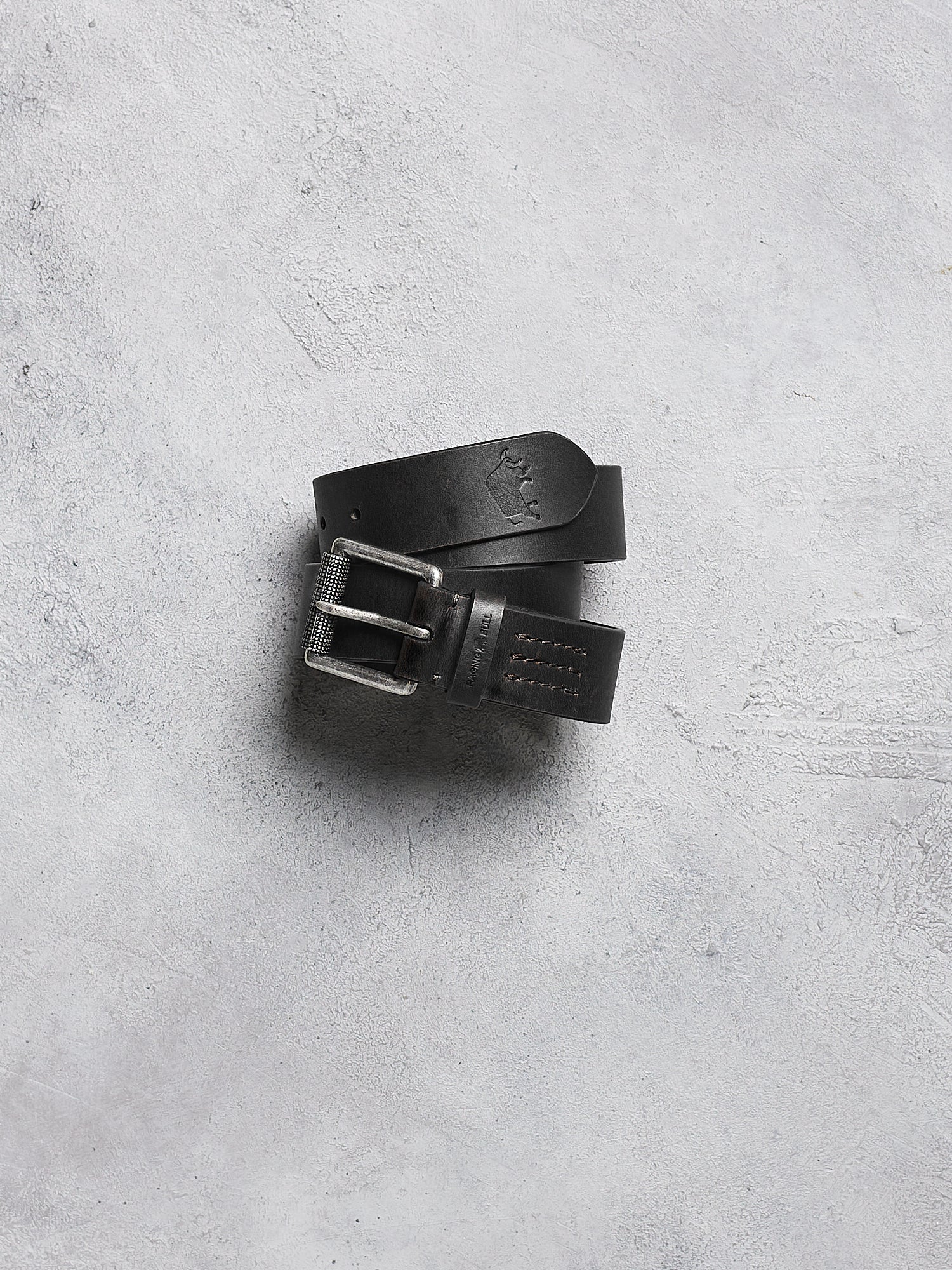Black leather belt with silver buckle on a gray concrete surface
