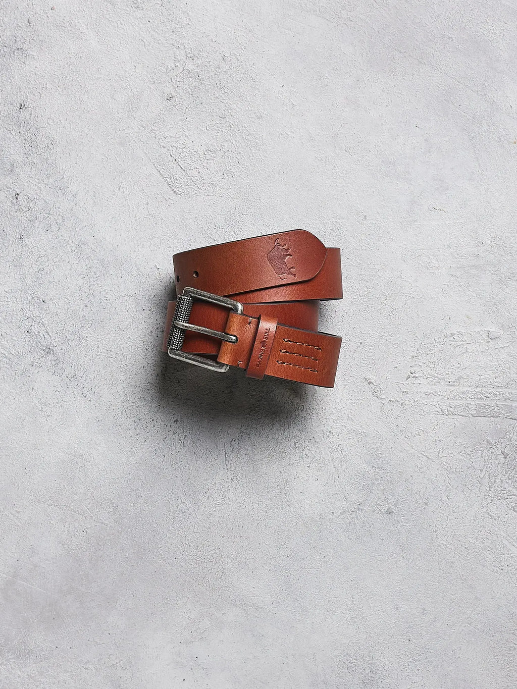 Brown leather belt with a silver buckle on a gray concrete surface