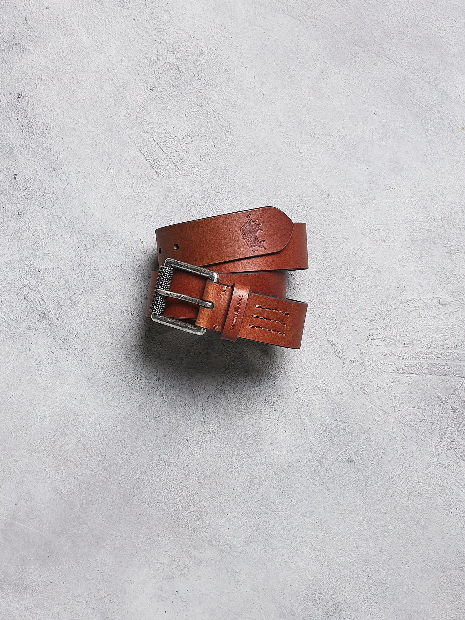 Brown leather belt with a silver buckle on a gray concrete surface