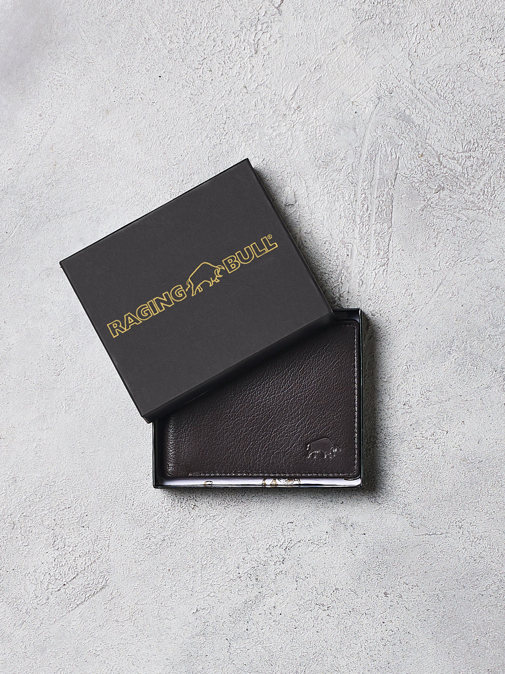 Brown leather wallet with 'Raging Bull' branding on a gray surface