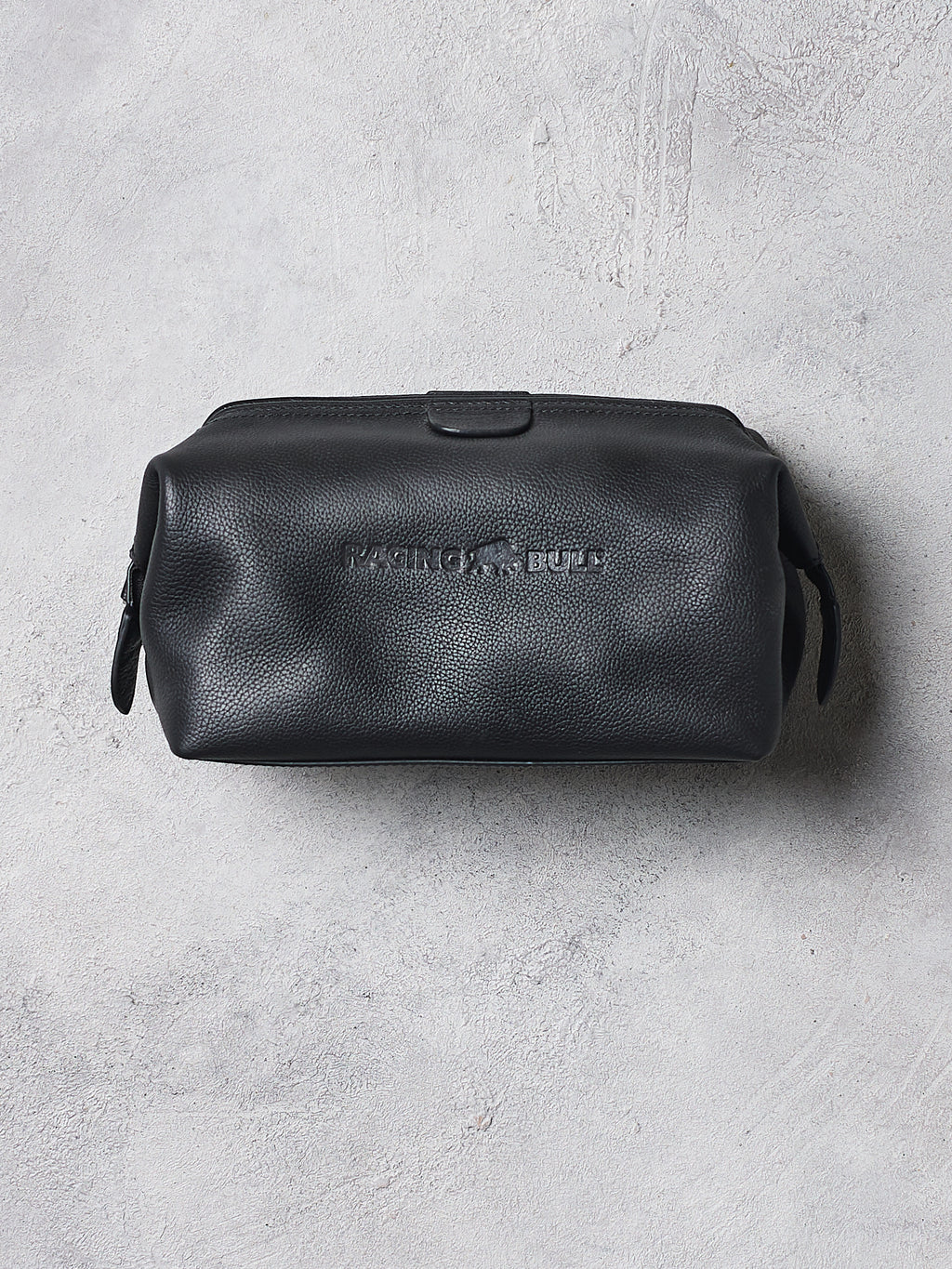 Black leather toiletry bag with brand logo on a gray concrete surface