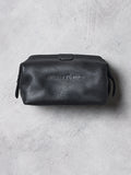 Black leather toiletry bag with brand logo on a gray concrete surface