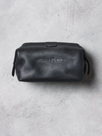 Black leather toiletry bag with brand logo on a gray concrete surface