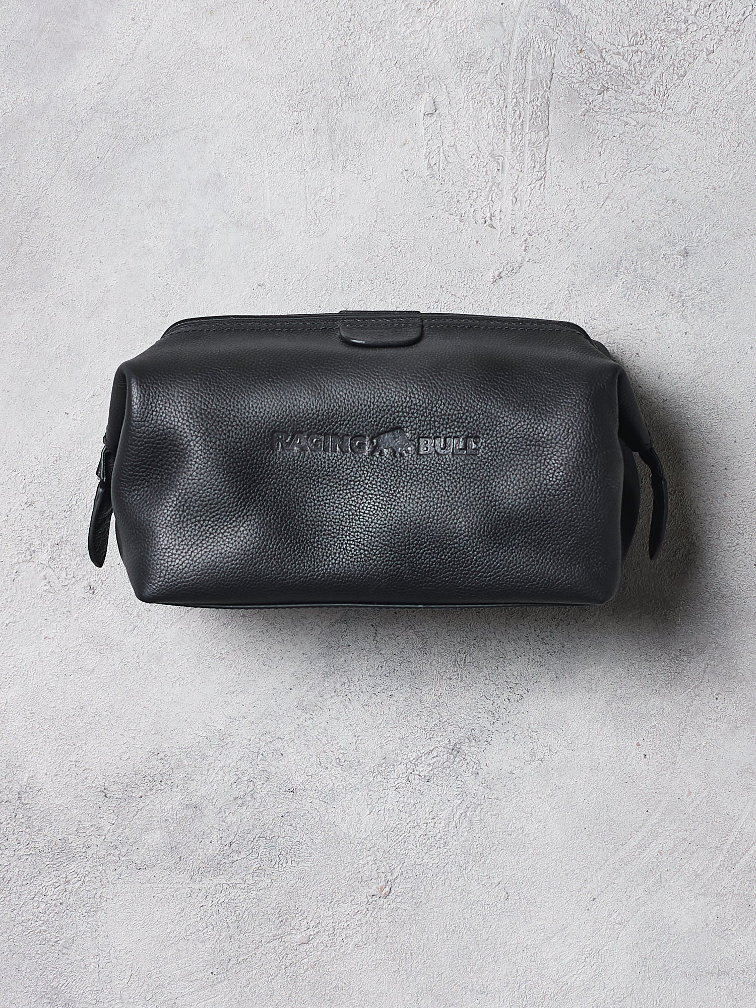 Black leather toiletry bag with brand logo on a gray concrete surface