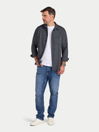 Man wearing a dark denim shirt over a white t-shirt, paired with blue jeans on a light gray background