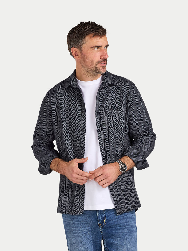 Man wearing a dark denim shirt over a white t-shirt on a light gray background