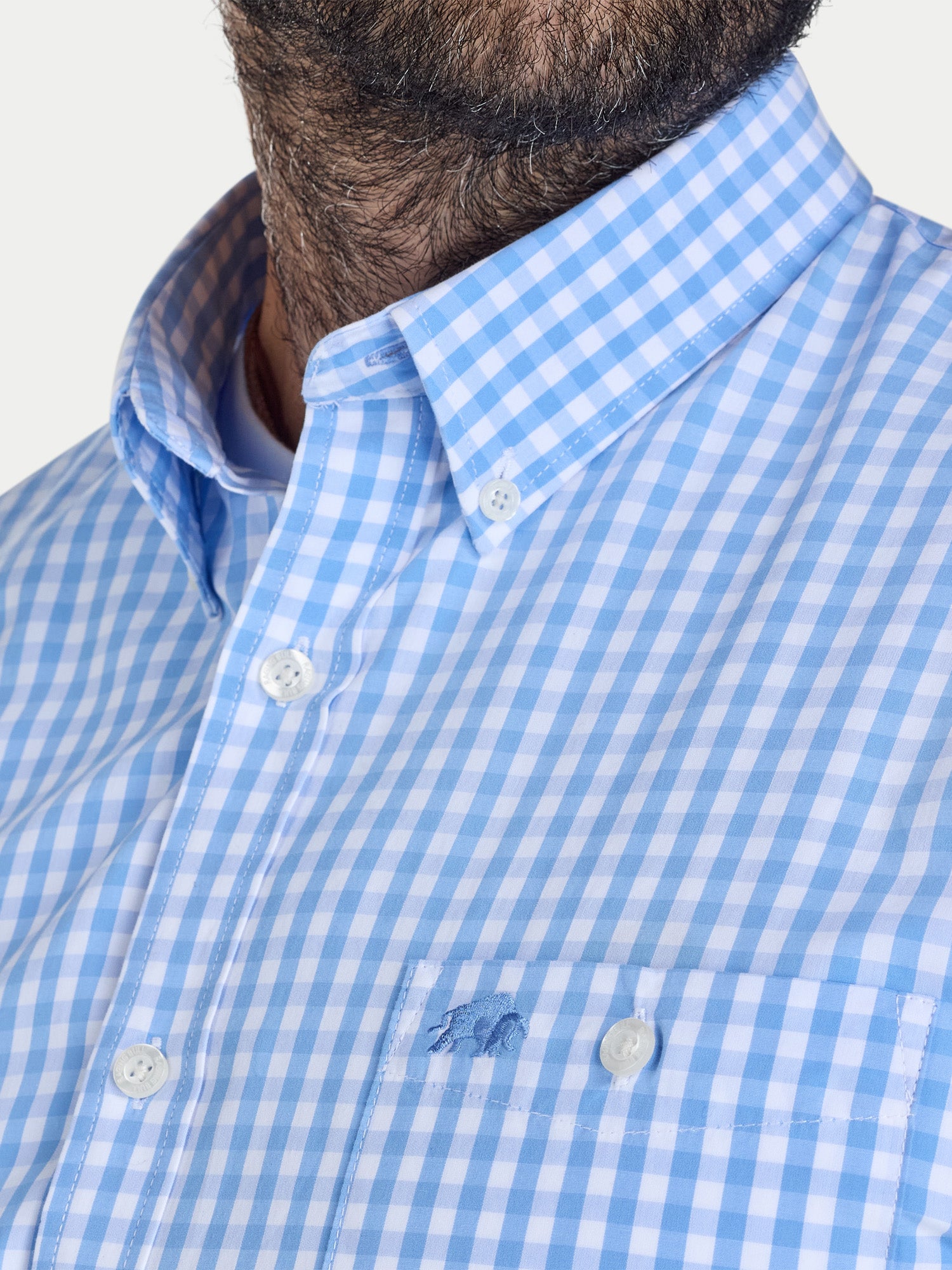 Close-up of a blue and white checkered shirt with a brand logo on a light gray background