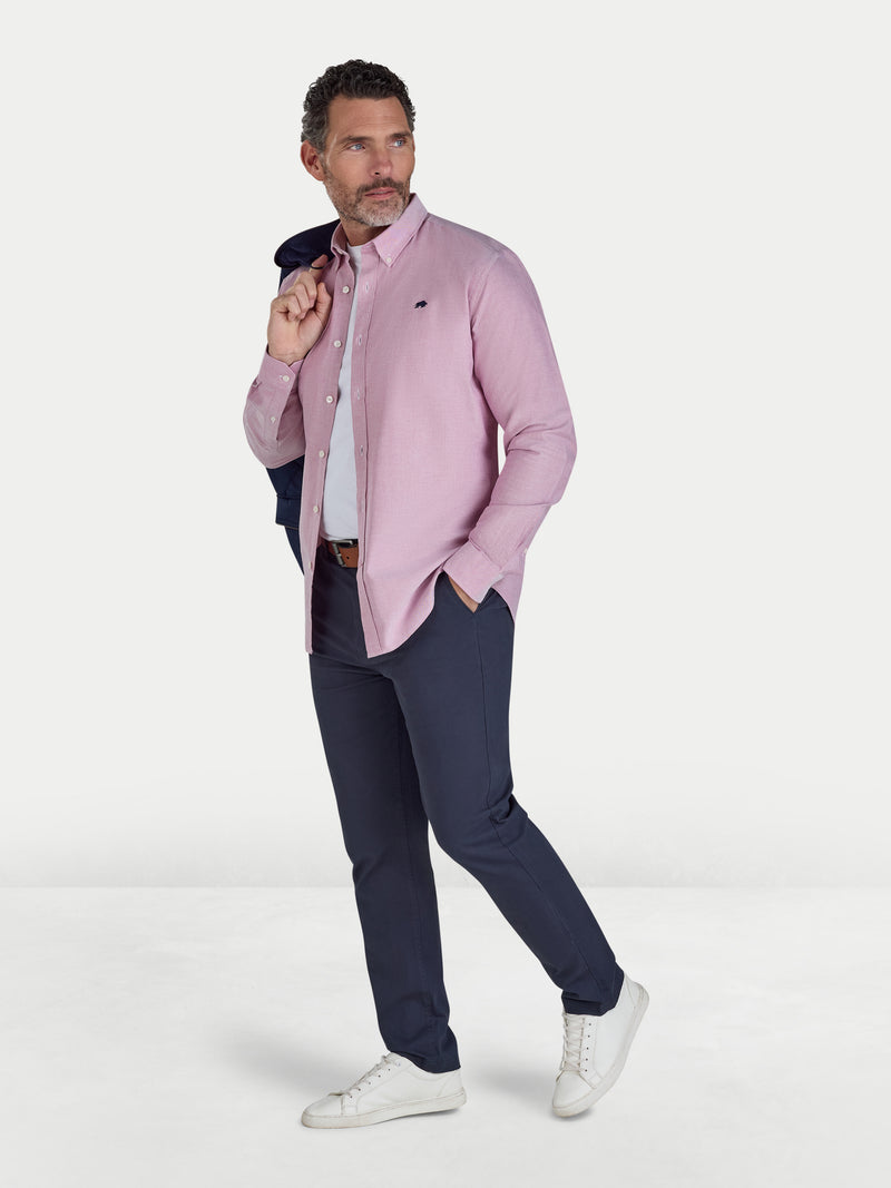 Man wearing a pink shirt, navy pants, and white sneakers on a white background