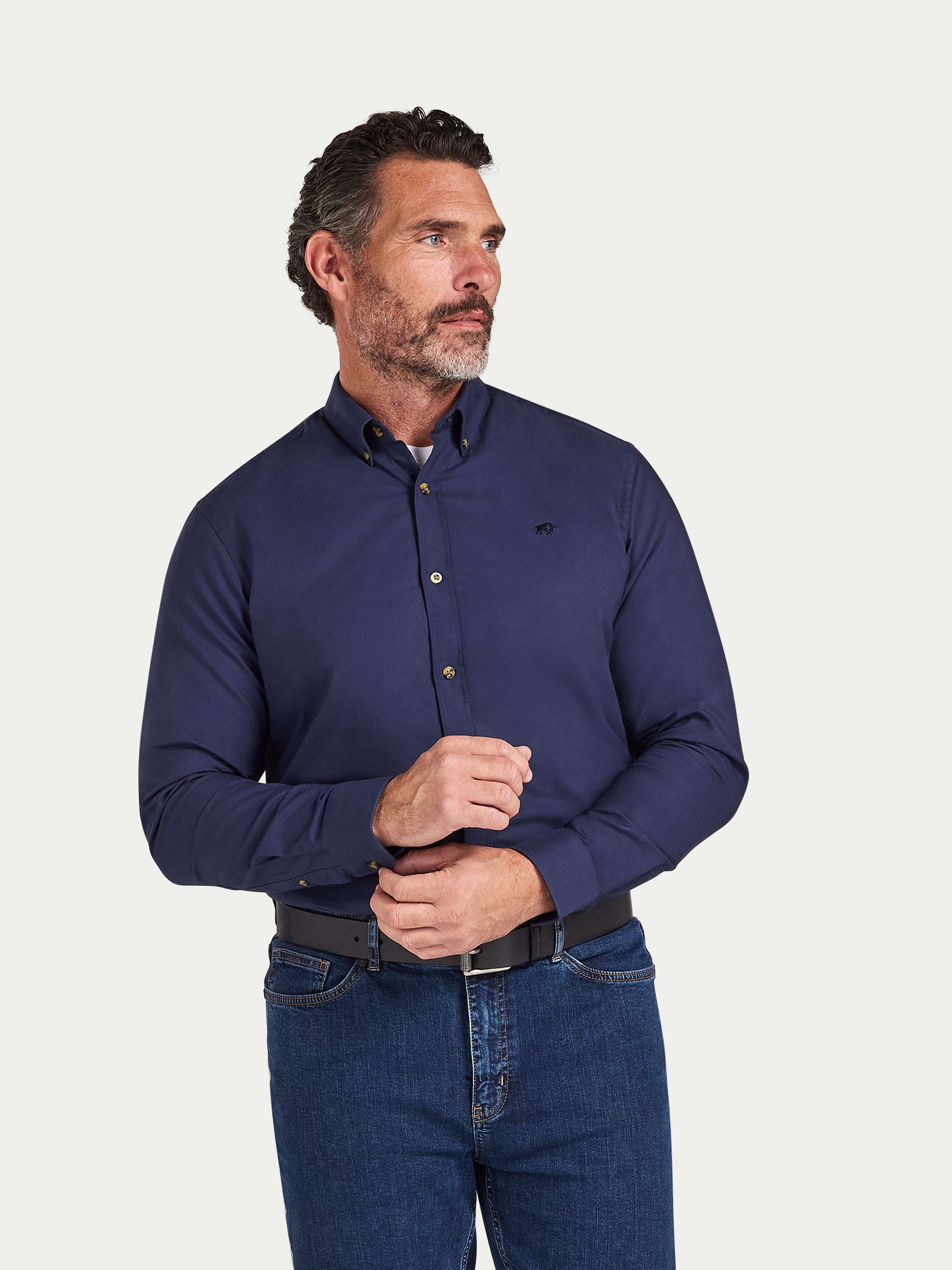 Man wearing a navy blue shirt and jeans on a light gray background