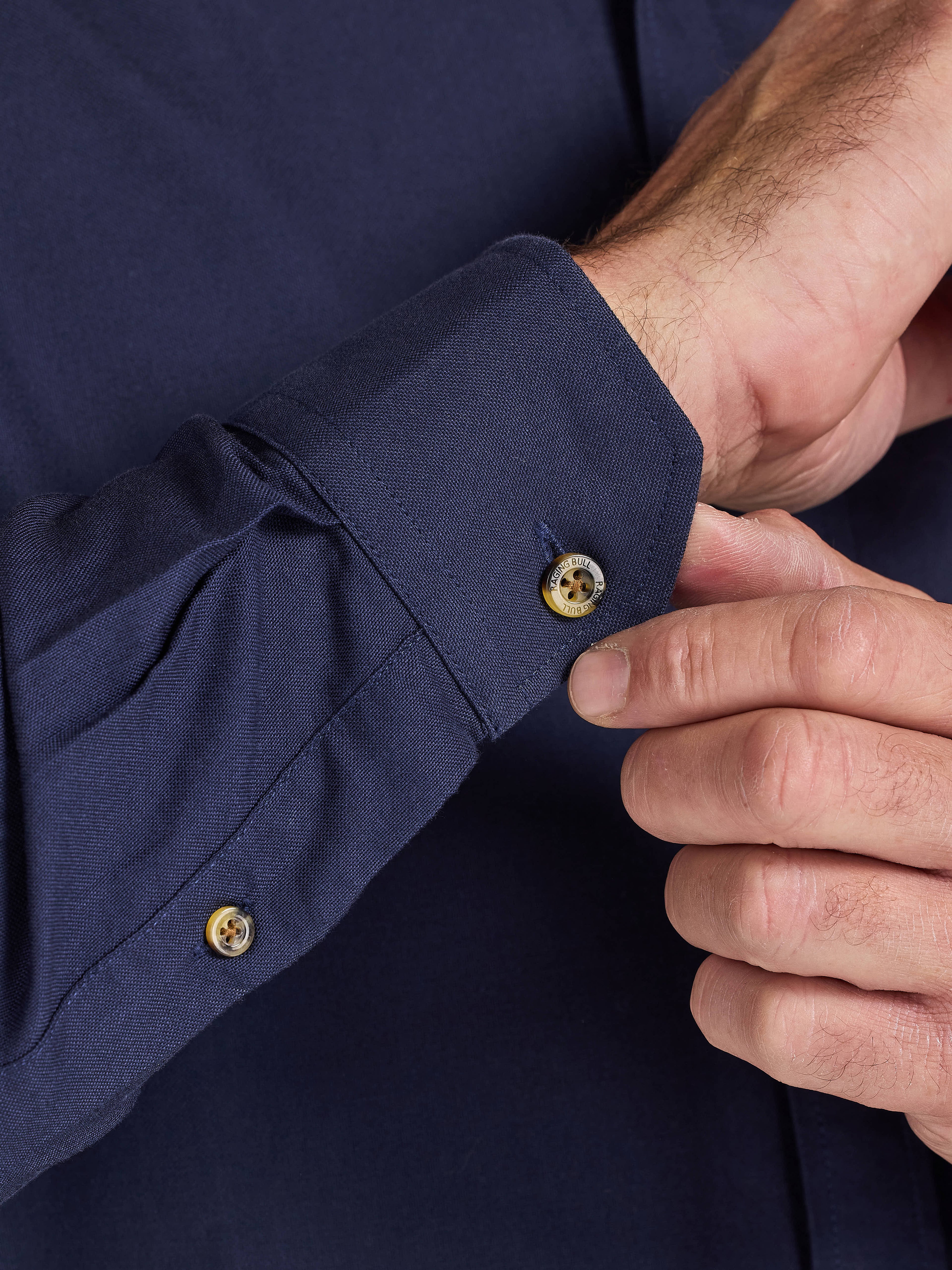 Close-up of a person adjusting the cuff of a Raging Bull Classic Oxford Long Sleeve Shirt in Navy, cuff detail, available in sizes S-6XL