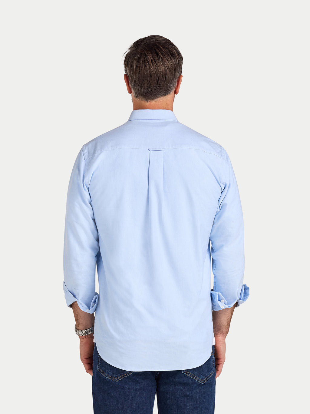 Man wearing a light blue shirt with rolled-up sleeves on a white background