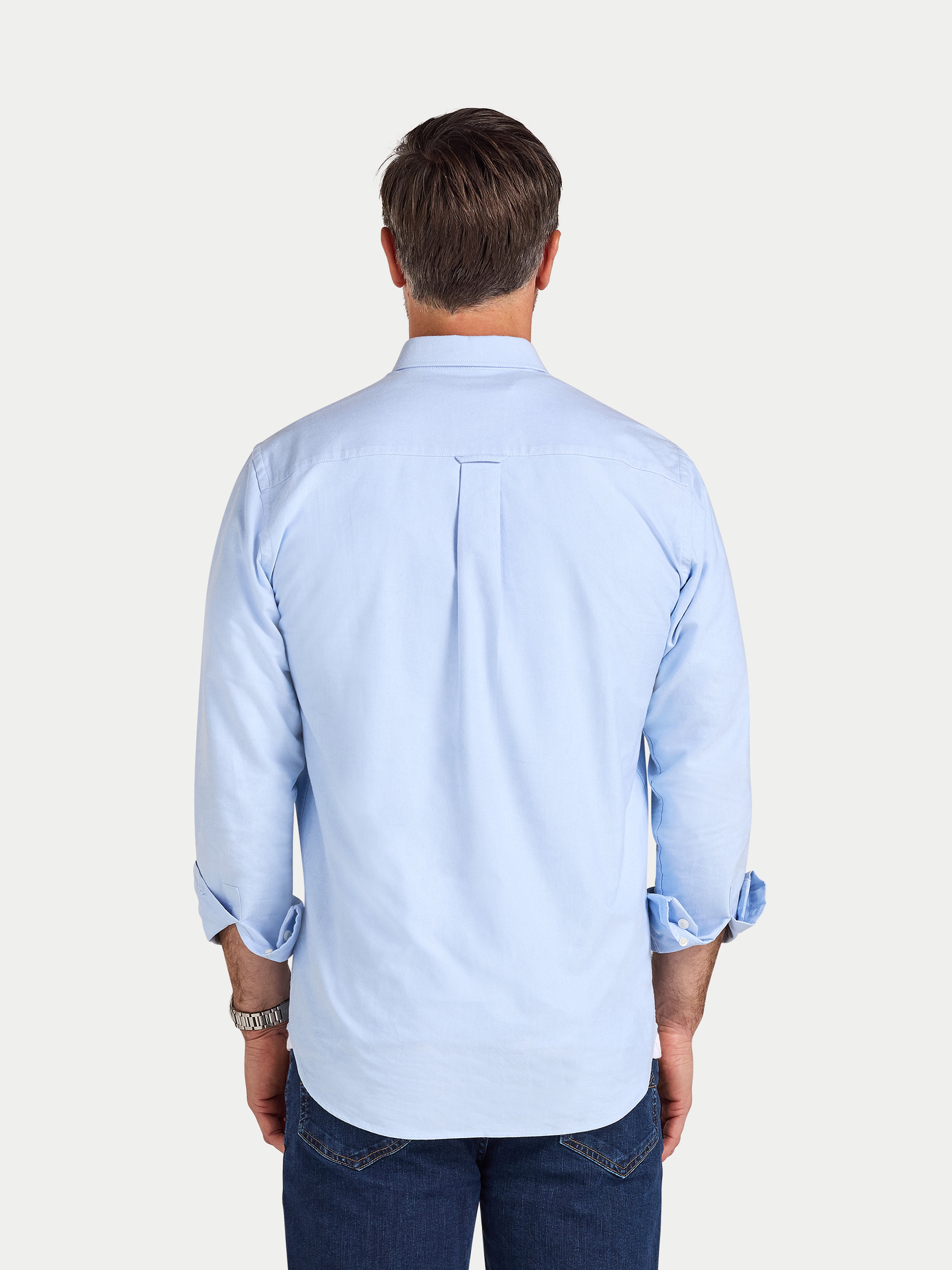 Man wearing a light blue shirt with rolled-up sleeves on a white background