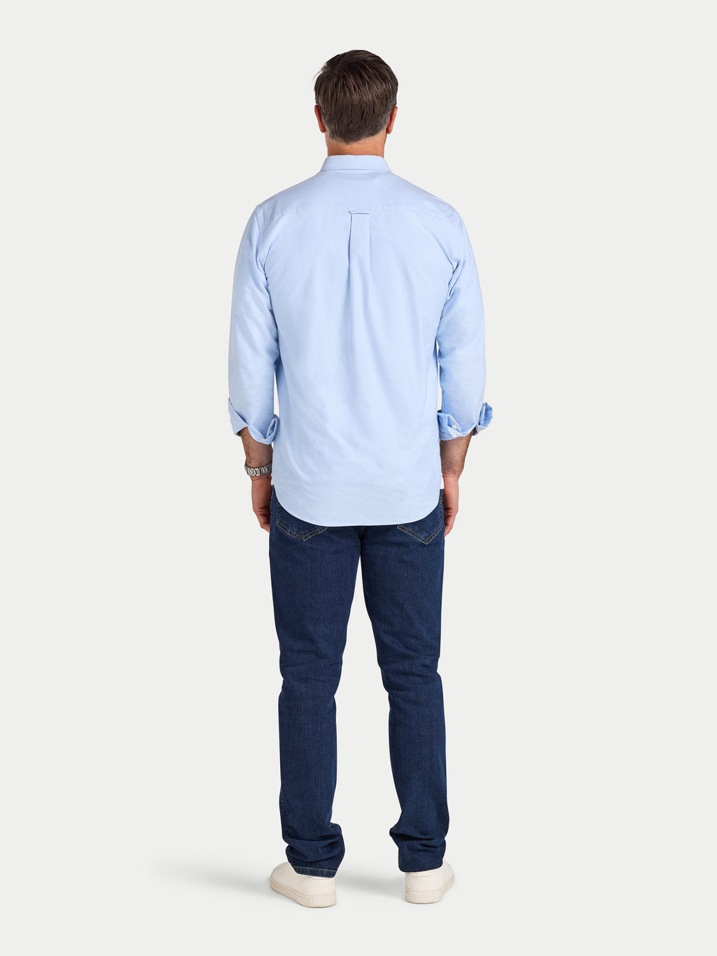 Man wearing a light blue shirt and dark blue jeans on a white background