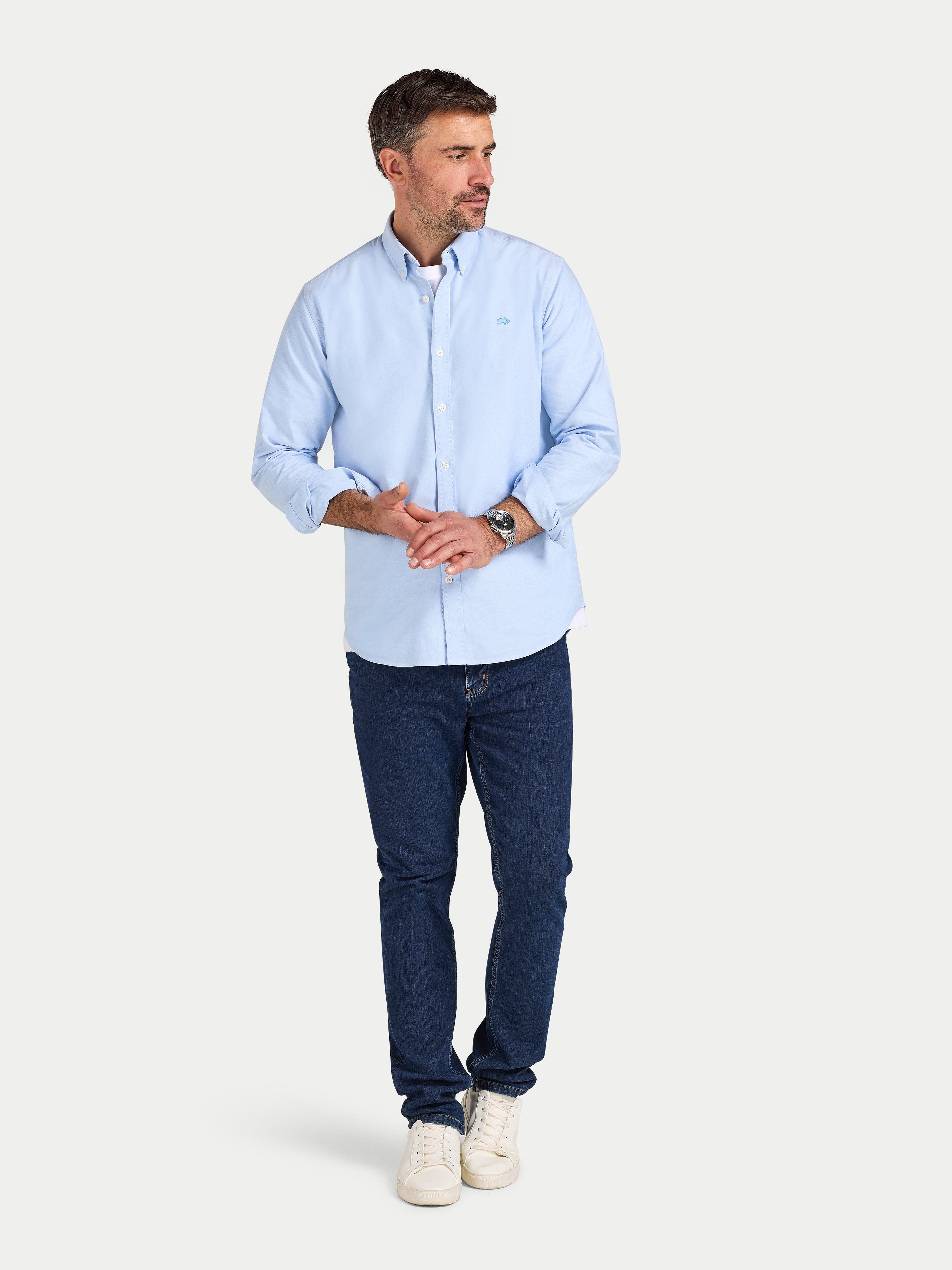 Man wearing a light blue shirt and dark blue jeans on a white background