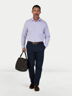 Man wearing a light purple checkered shirt and navy pants, holding a dark bag on a white background