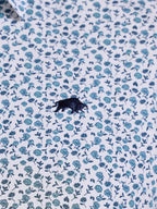 Close-up of a shirt with blue floral pattern and a black logo.