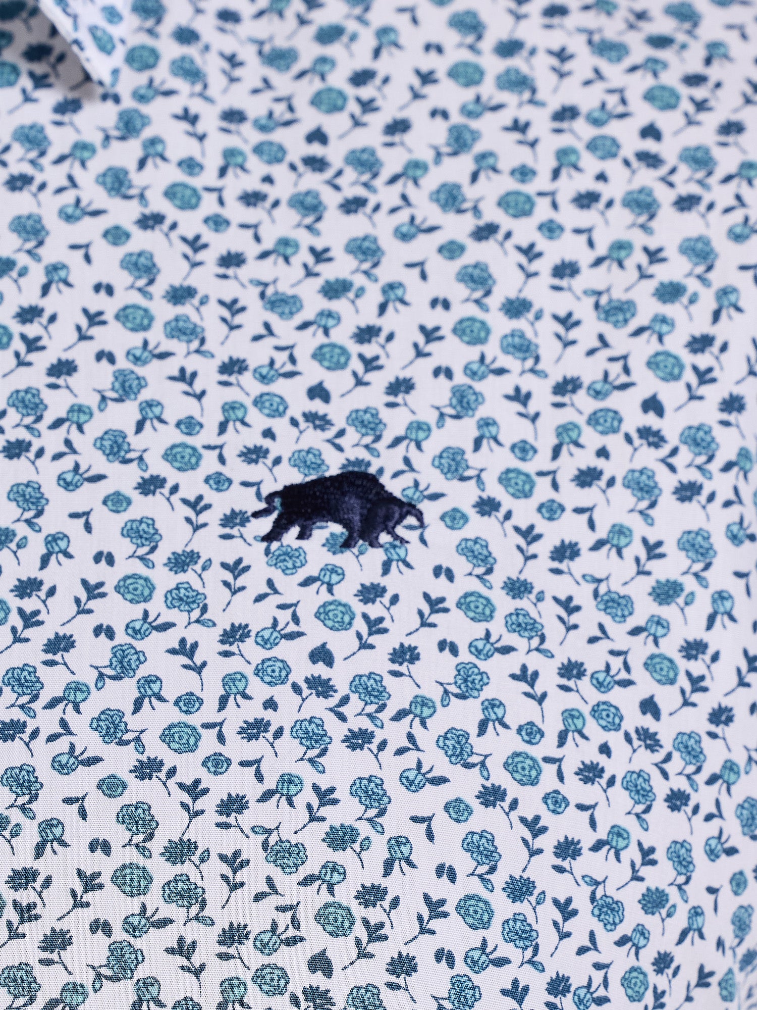 Close-up of a shirt with blue floral pattern and a black logo.