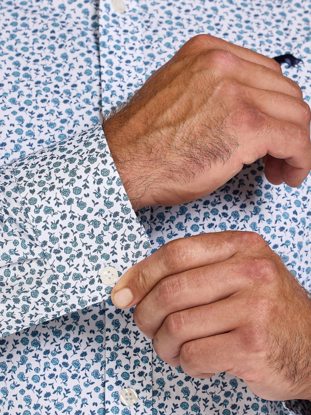 Close-up of a person adjusting the cuff of a floral-patterned shirt.