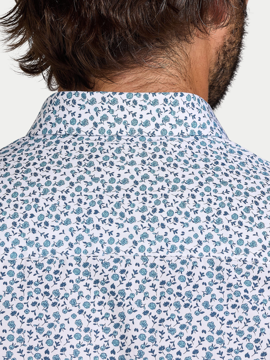 Close-up of a person wearing a floral patterned shirt with blue flowers on a white background.