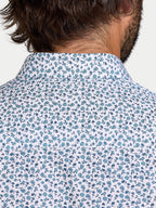 Close-up of a person wearing a floral patterned shirt with blue flowers on a white background.