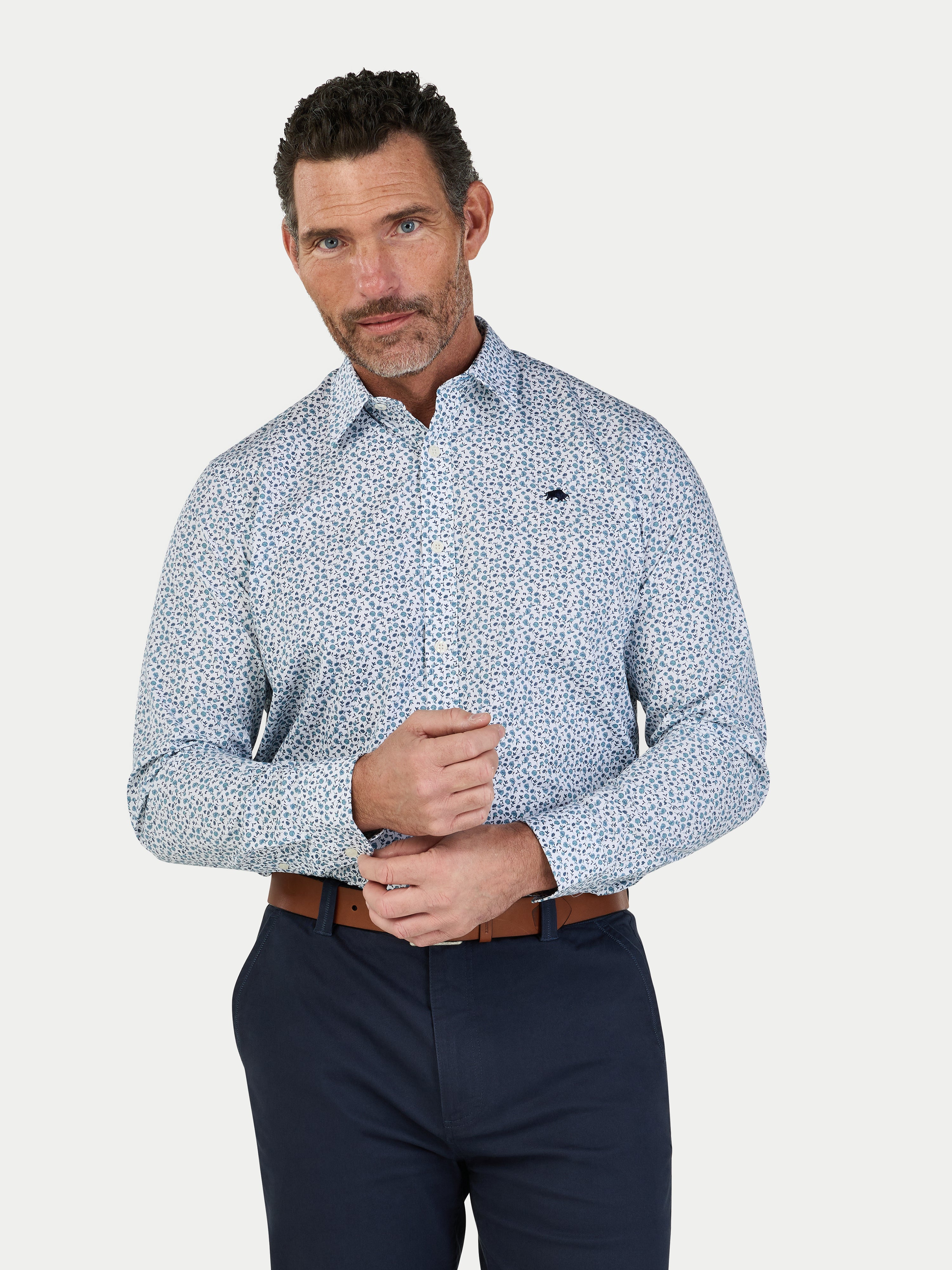 Man wearing a patterned shirt and dark pants on a light gray background