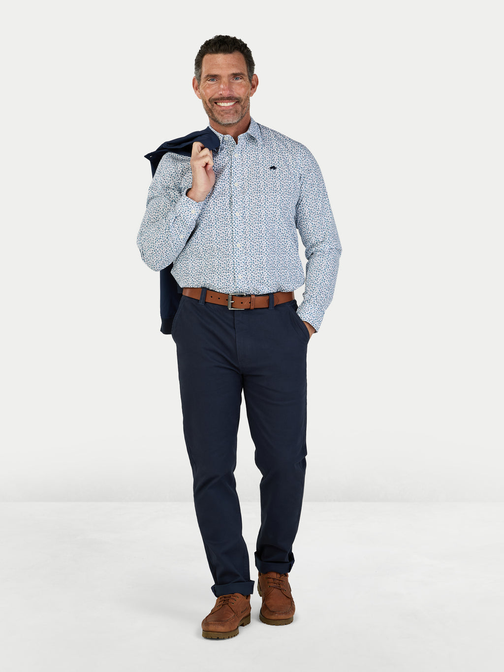 Man wearing a patterned shirt, navy pants, and brown shoes on a white background